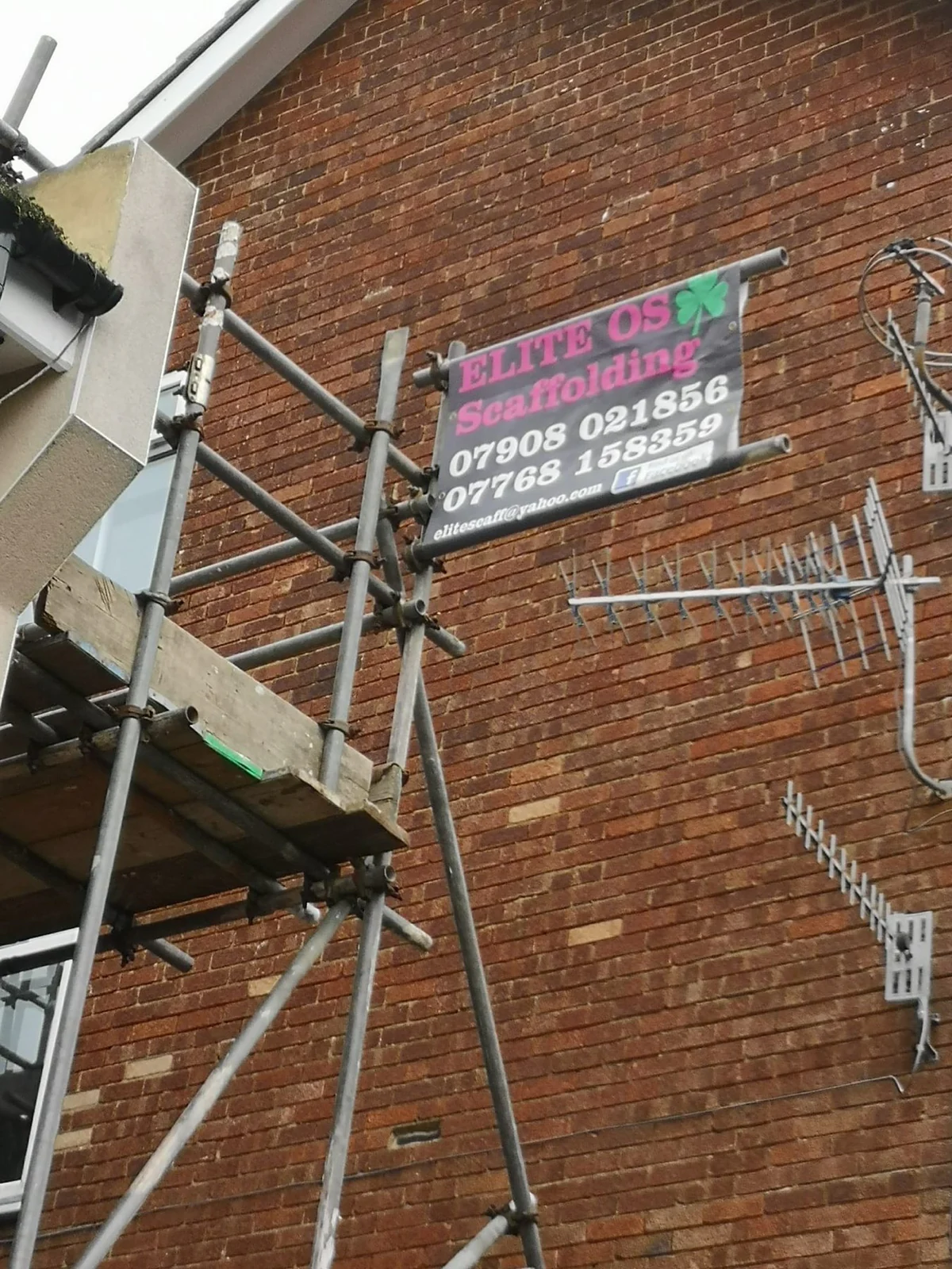 Elite Scaffolding site board fixed to scaffold tubes on a brick wall