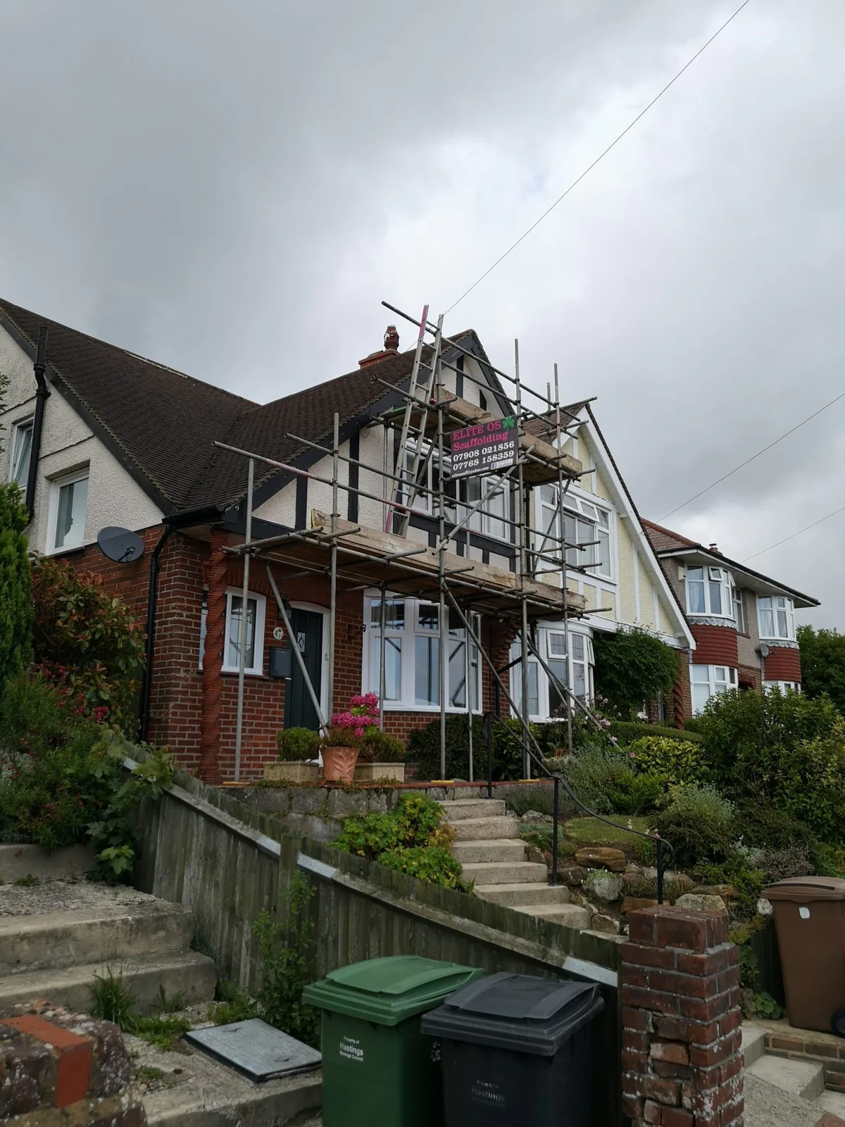 Scaffold on a Hastings house with an Elite site board and wheelie bins in front